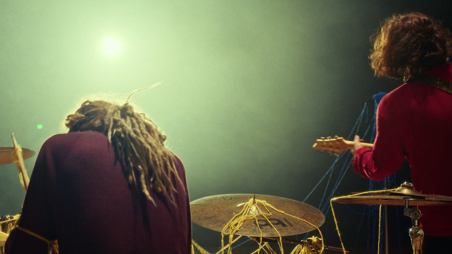 Brian (Left) and Mason (Right) on stage with a drum set and guitar, illuminated by a spotlight during Thread music video